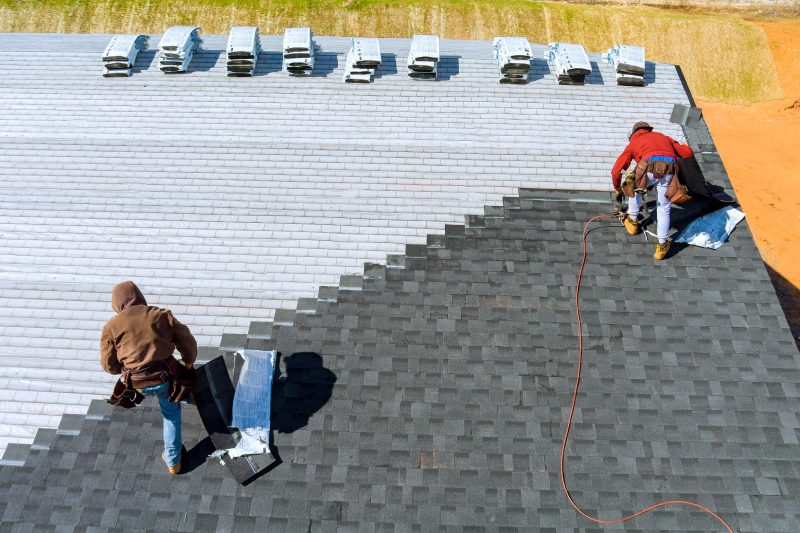 Two roofers installing asphalt shingles on a roof.
