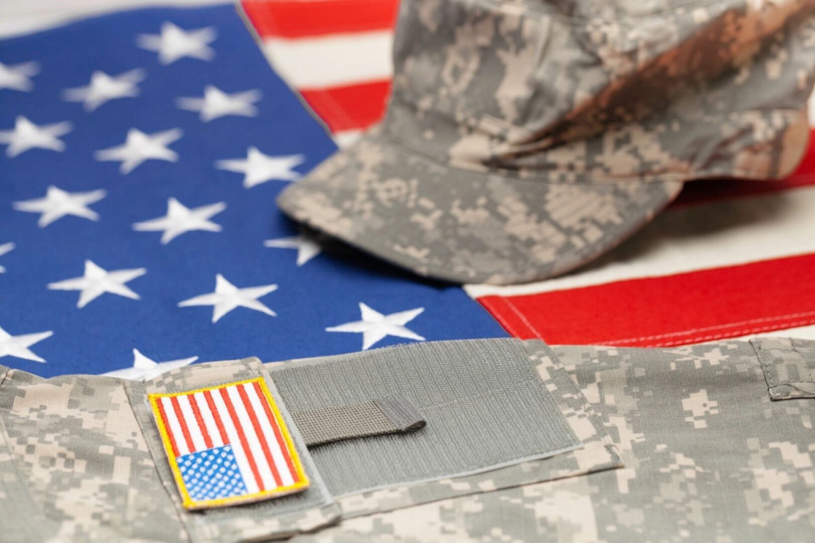 A camouflage cap and uniform on an American flag.
